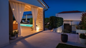 Une maison moderne avec une piscine, des rideaux blancs et des plantes en pot.