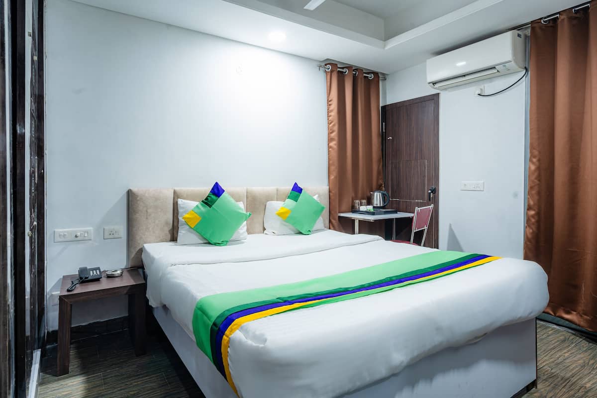 A hotel room with a bed, a desk, a chair, an air conditioning unit, and a window with curtains.
