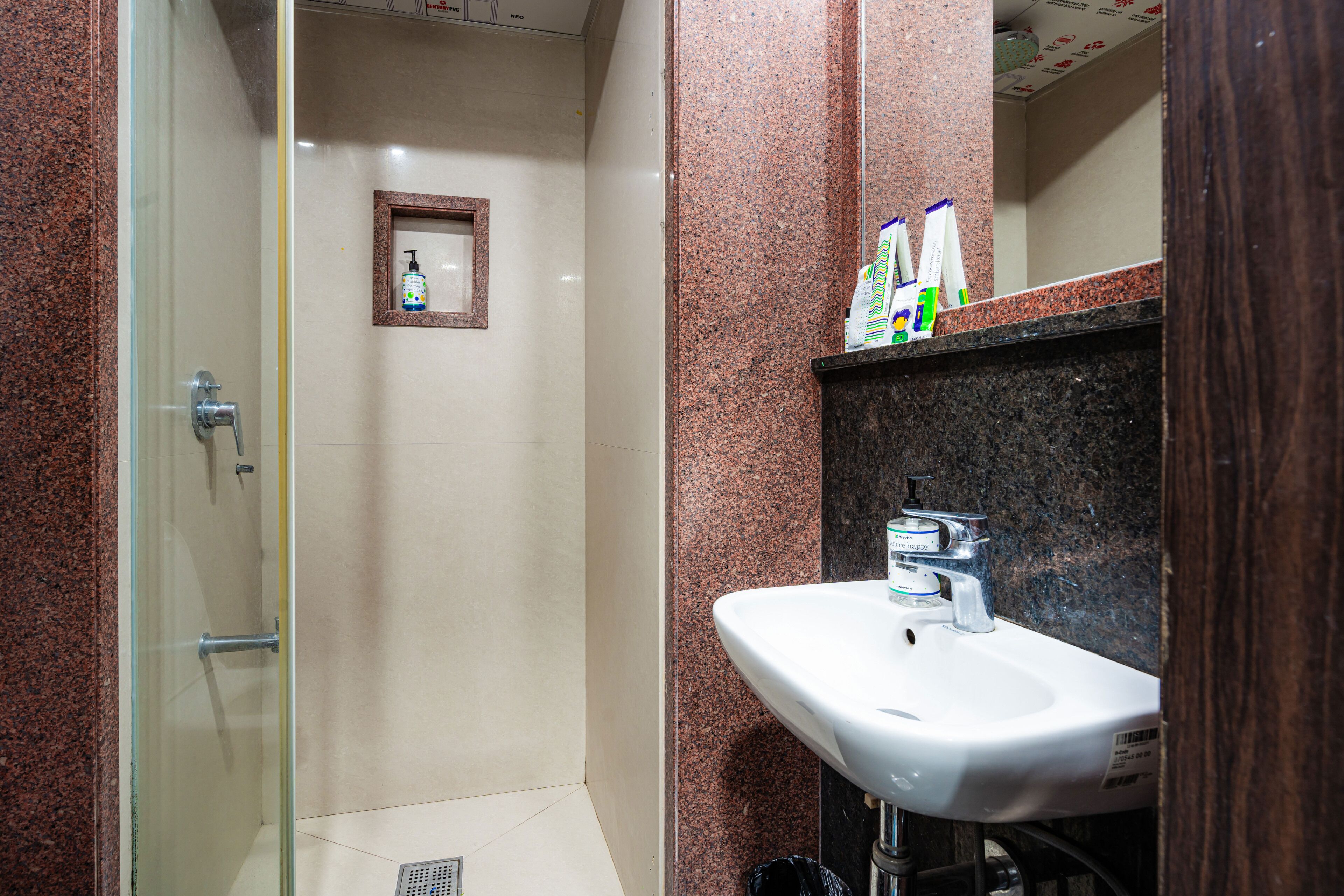 Un baño con mampara de vidrio, un lavamanos blanco y artículos de tocador en la encimera.