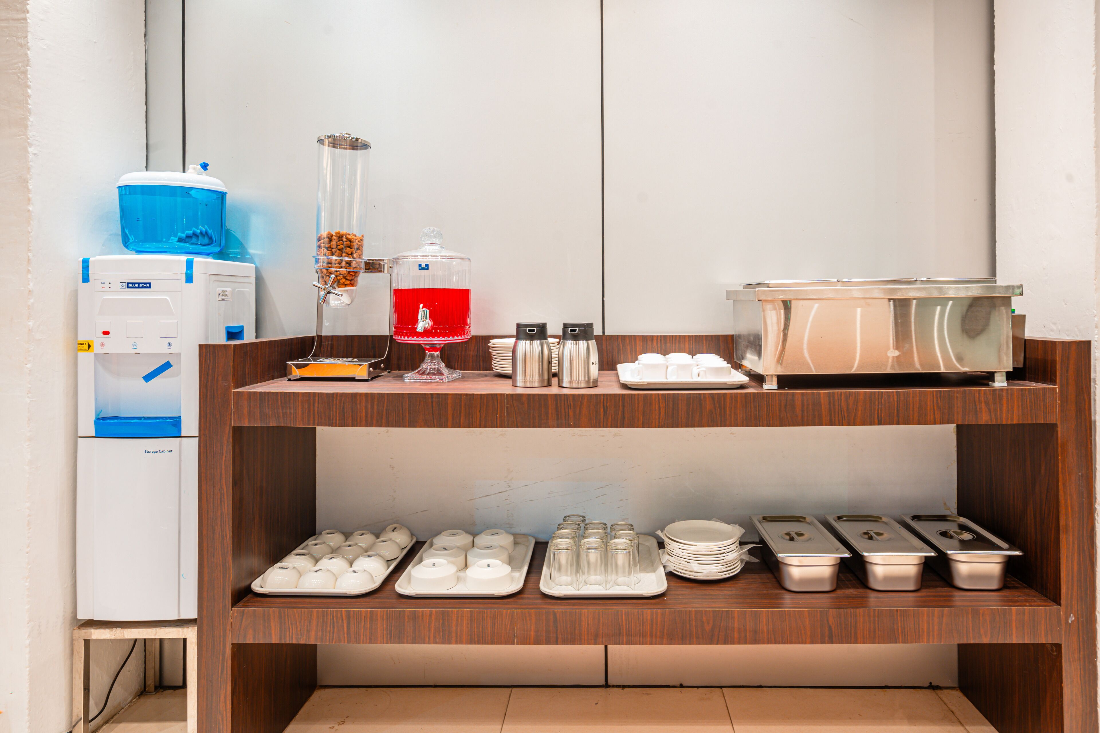 Disposição de buffet com dispensadores de água, um dispensador de bebidas e diversos recipientes de comida sobre prateleiras de madeira.