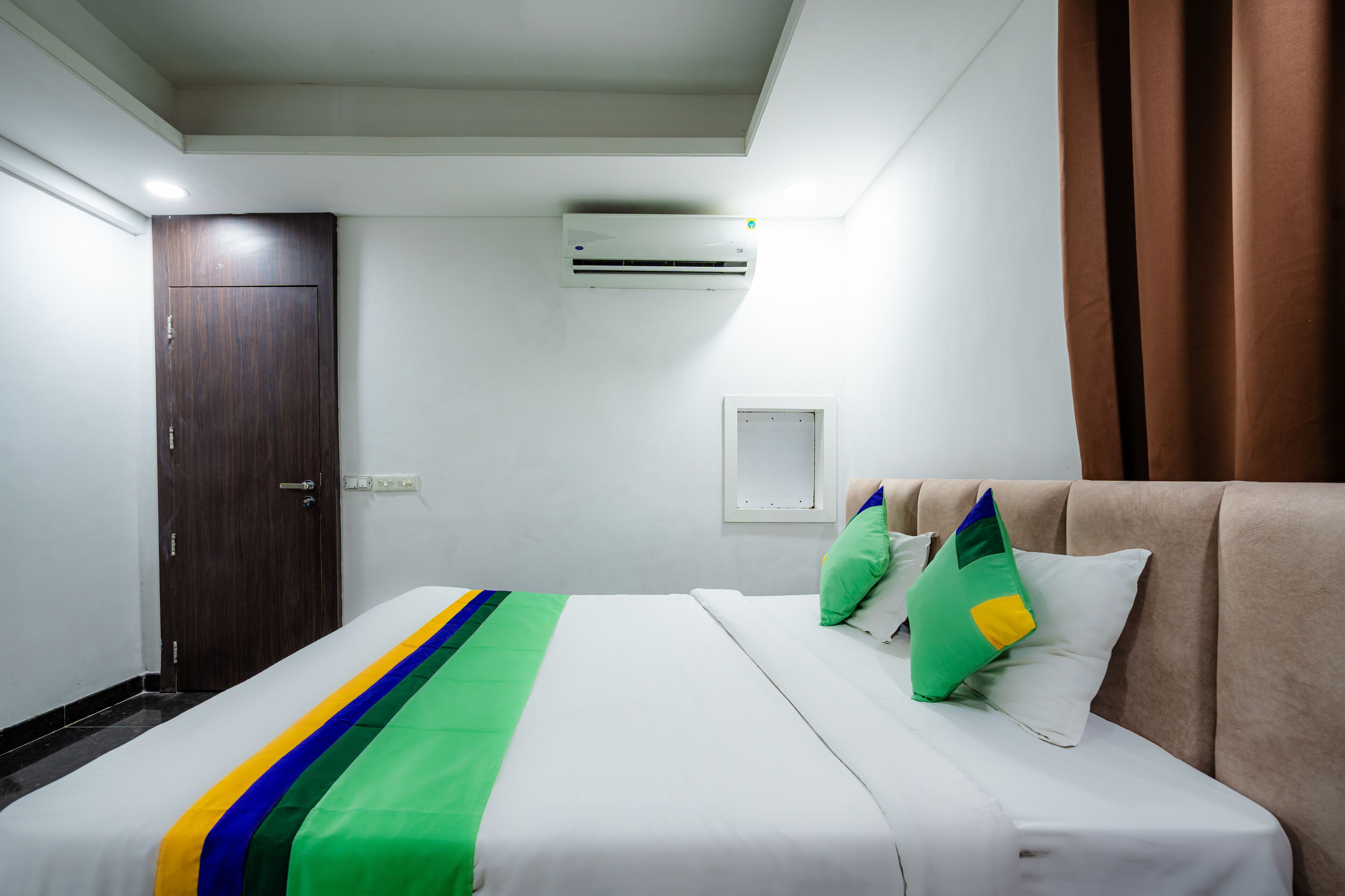 Una habitación de hotel con cama, armario, aire acondicionado y ventana con cortinas.