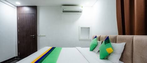 Una habitación de hotel con cama, armario, aire acondicionado y ventana con cortinas.