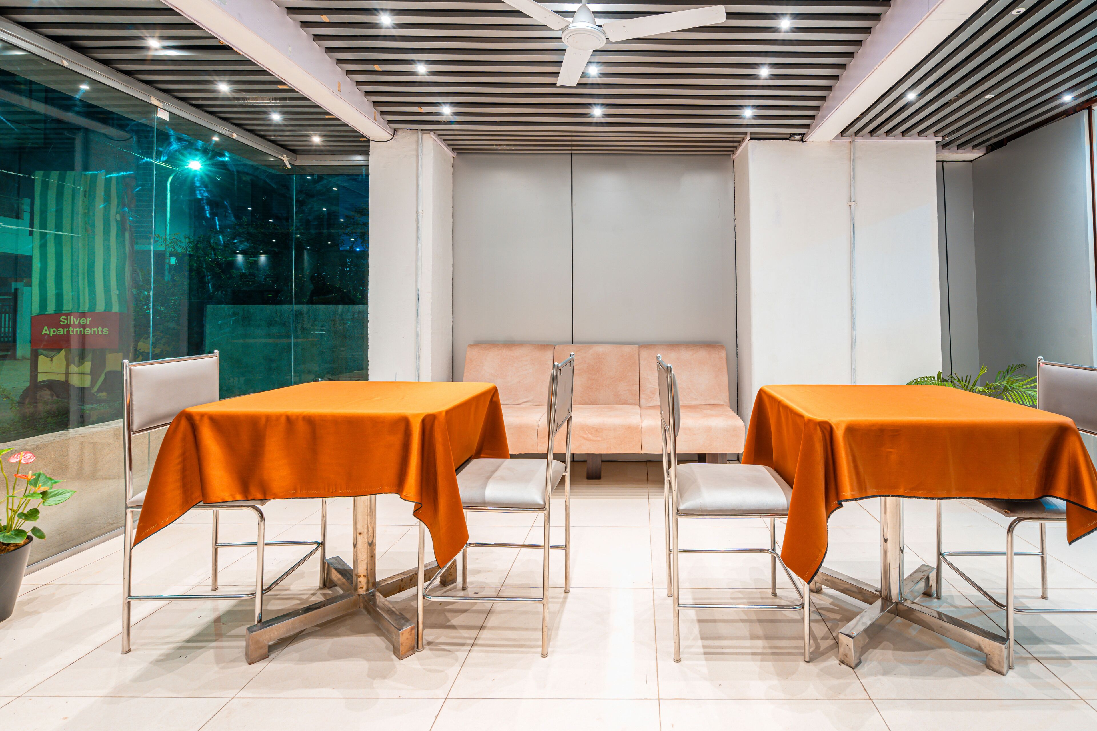 A modern dining area with two tables covered in orange tablecloths, surrounded by metal chairs.