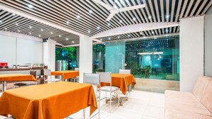 Un comedor moderno con mesas cubiertas con manteles naranjas, sillas de metal y una pared divisoria de vidrio.