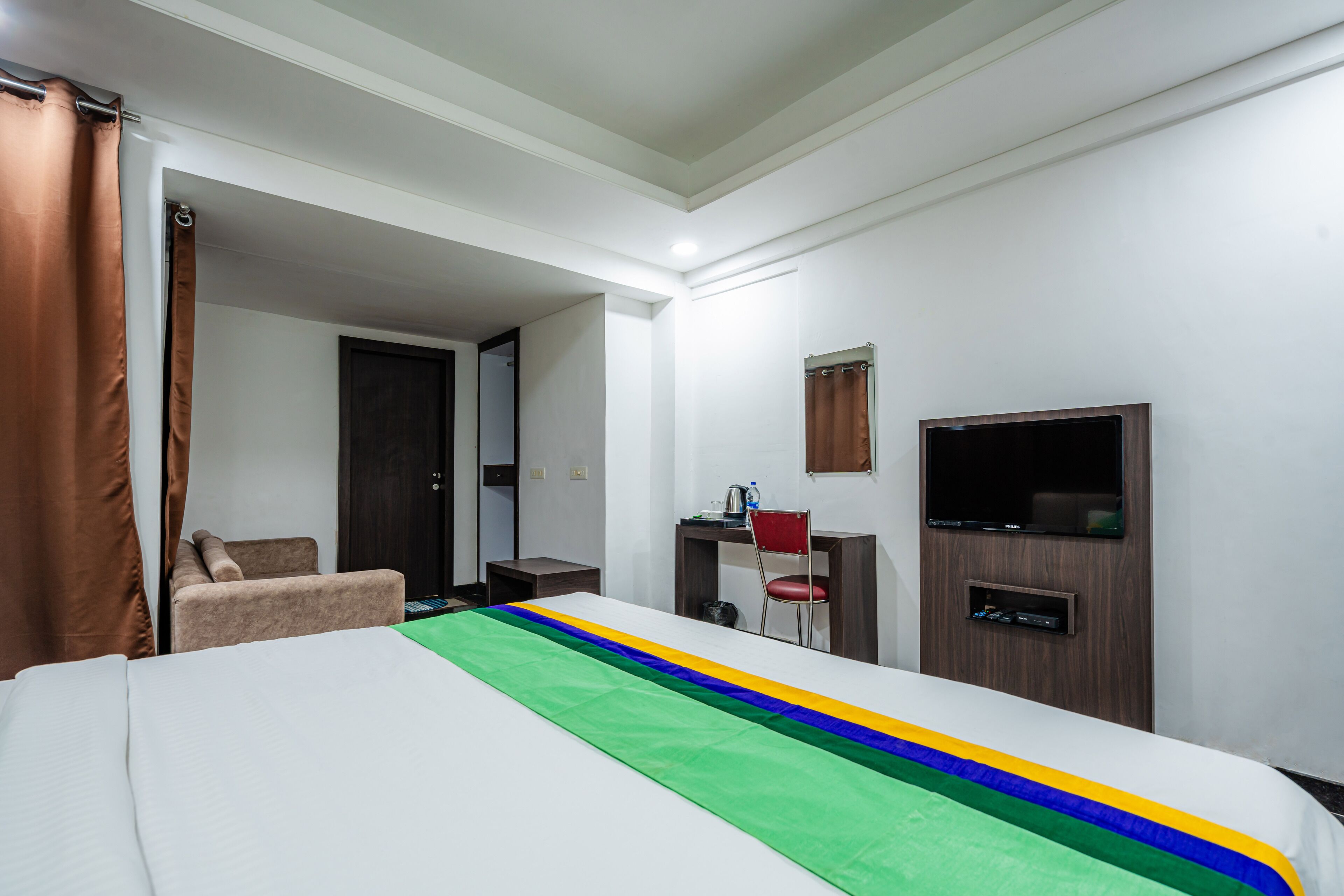 Una habitación de hotel con cama, escritorio, silla, televisor y puerta de baño.