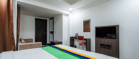 Una habitación de hotel con cama, escritorio, silla, televisor y puerta de baño.