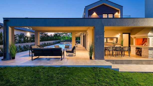 Une maison moderne dotée d’un espace extérieur couvert, d’une piscine et d’une cheminée.
