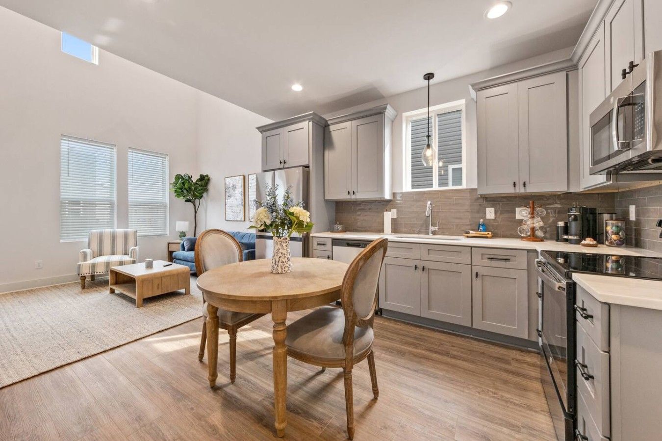 A modern kitchen with grey cabinets, a wooden dining table, and a built-in oven.