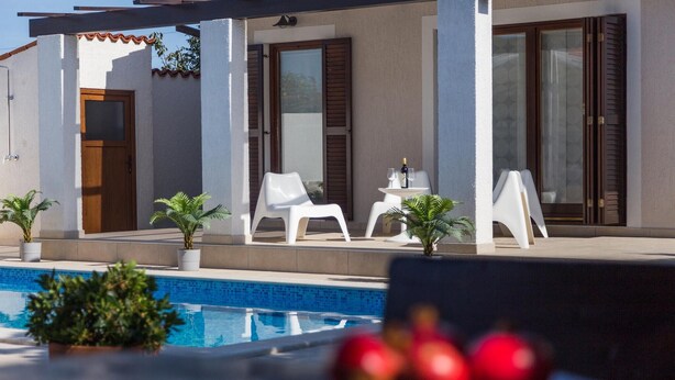 A modern outdoor pool area with a clear view of the pool, white lounge chairs, and potted plants. - Beach front home in Pula (Pula)