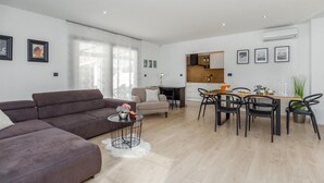 A modern living room with a brown sofa, a dining area with a wooden table and chairs, and a kitchen area with a wooden countertop and cabinets. - Beach front home in Pula (Pula)