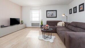 A modern living room with a flat-screen TV, a brown sofa, a small round table with candles, and a large window. - Beach front home in Pula (Pula)