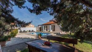 A pool area with lounge chairs, a wooden bench with fruit, and a building with a tiled roof. - Beach front home in Pula (Pula)