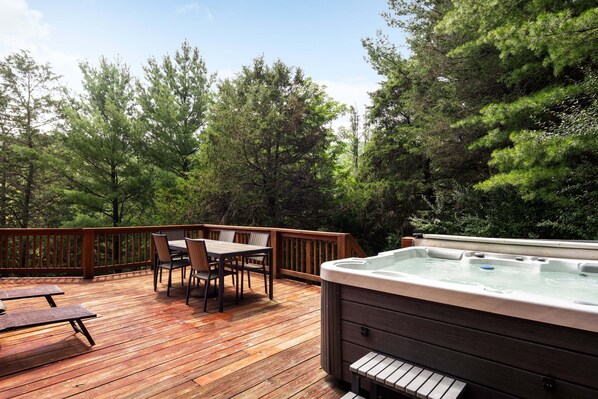 A wooden deck with a hot tub, a table, and chairs, surrounded by trees. - Entire Cabin in Lost River w/ fire pit + pet friendly! (Lost River)