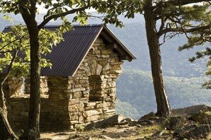 Une cabane en pierre, dotée d’un toit en pente, entourée d’arbres et offrant une vue sur un paysage montagneux.
