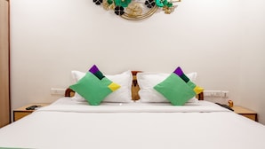 Cama bem arrumada com roupa de cama branca e duas almofadas com detalhes em verde, roxo e amarelo.
