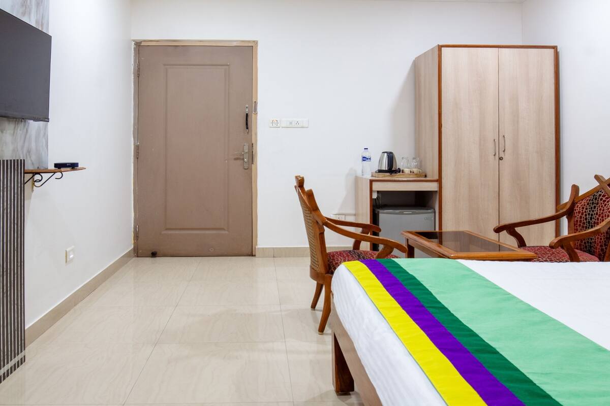 A hotel room with a bed, a wooden wardrobe, a small table with chairs, a television mounted on the wall, and a radiator.
