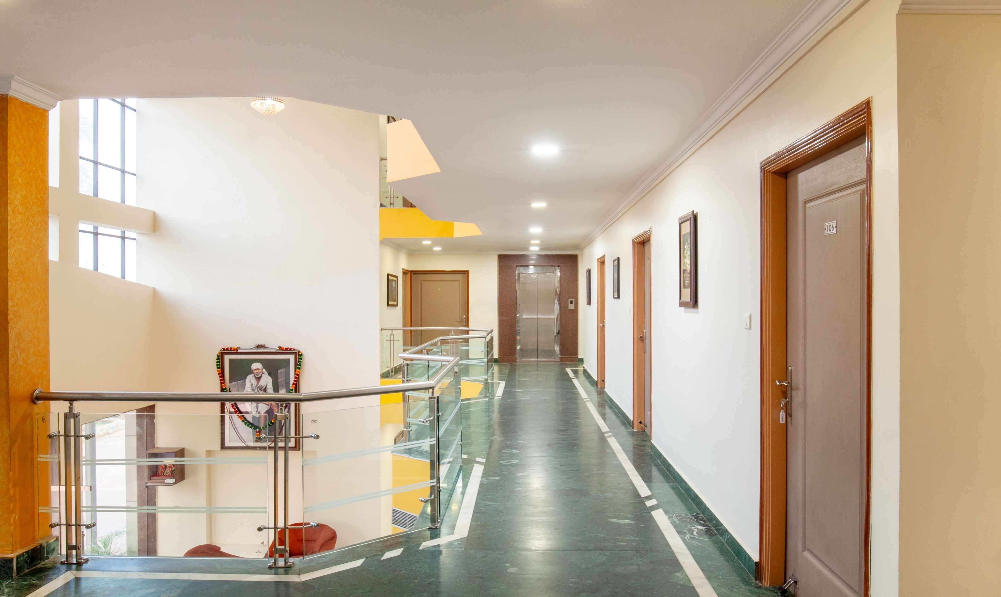 Un pasillo de hotel con barandilla de vidrio, un cuadro enmarco y puertas que dan a habitaciones.