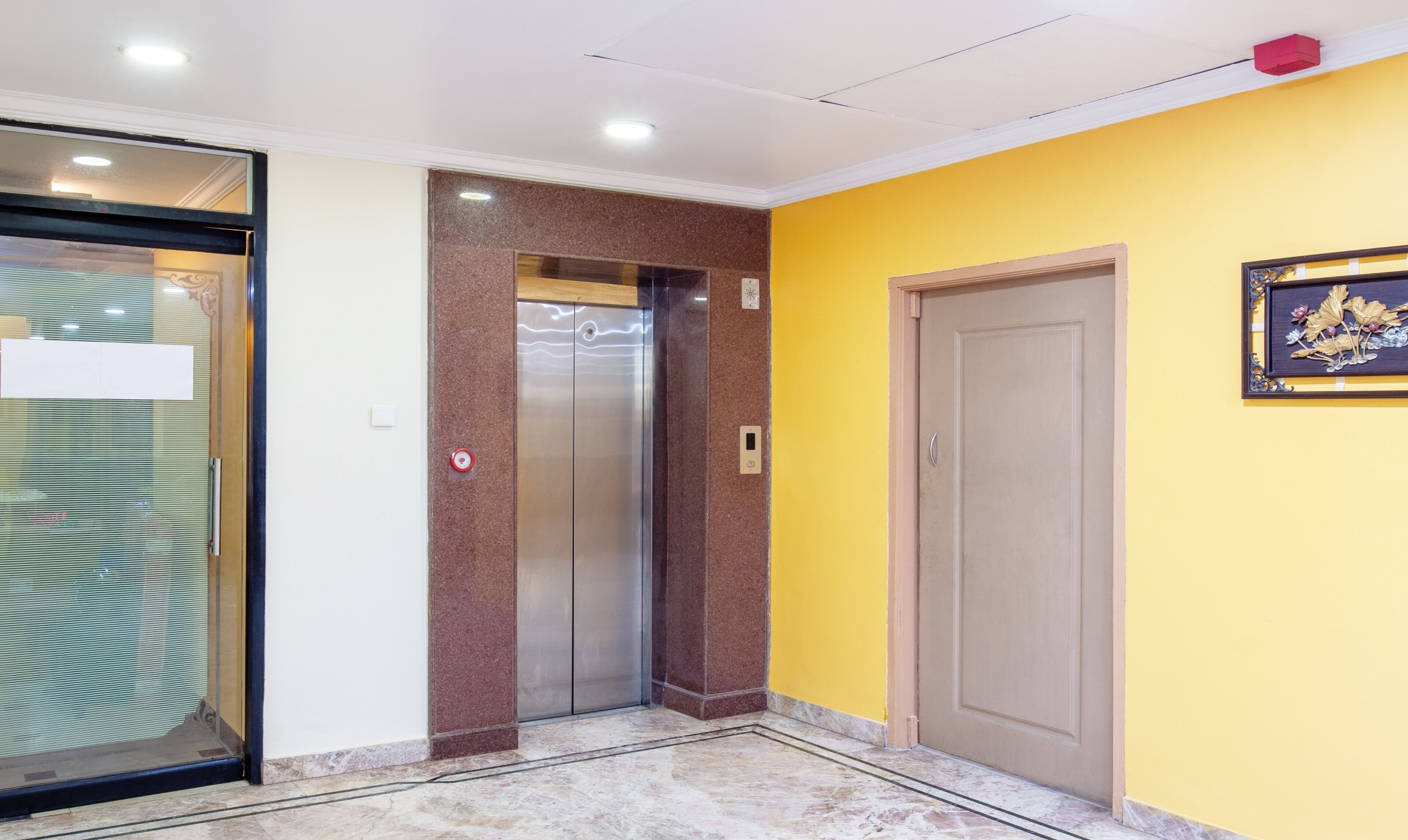 An elevator in a building with a yellow wall and a door with a decorative frame.