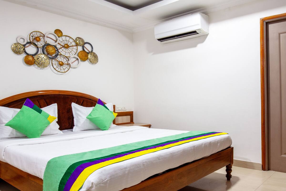 A neatly made bed with a colorful striped blanket, a wooden headboard, and a wall-mounted air conditioner.