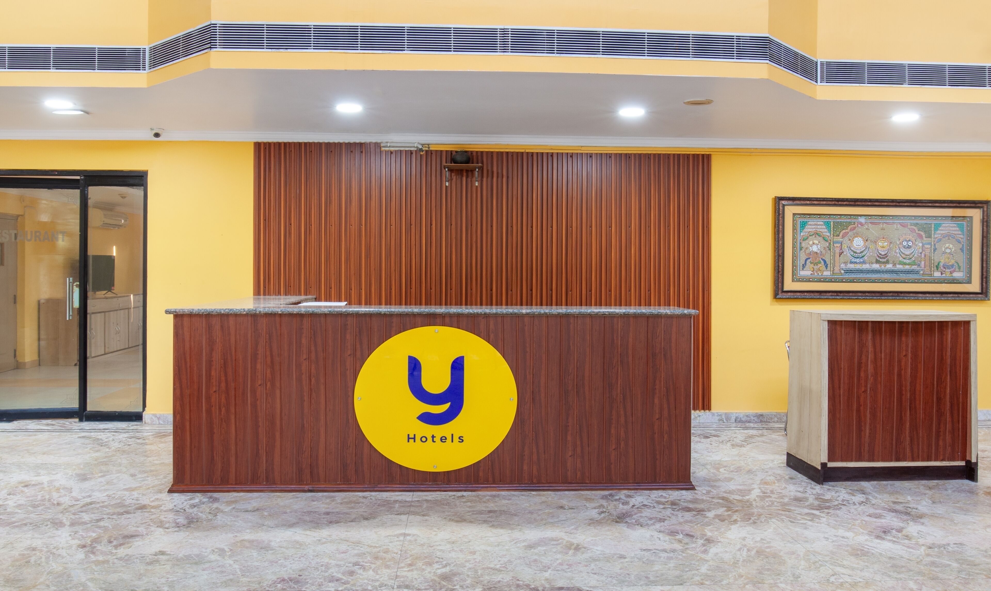 A reception desk with a logo, a wooden panel wall, a framed artwork, and a marble floor.