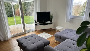 Uma sala de estar moderna com um sofá cinzento, um banquinho e uma TV de tela plana sobre um suporte branco.