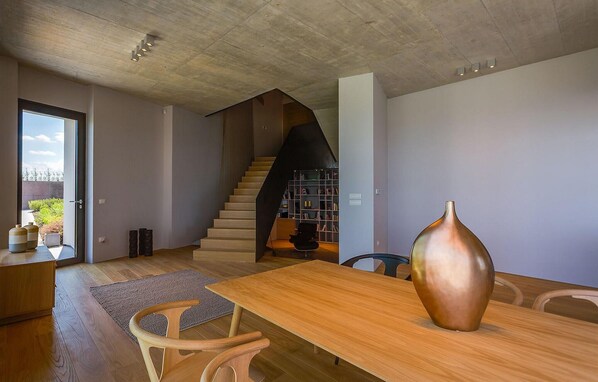 Un intérieur moderne avec une table à manger en bois, un grand vase et un escalier menant à une bibliothèque.
