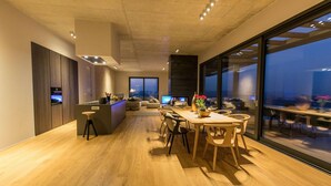A modern kitchen with a central island, a dining area with wooden furniture, and large windows offering a view of the city at night. - Luxurious home in Pazin (Pazin)
