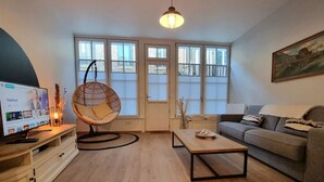 A modern living room with a sofa, a wooden coffee table, a hanging chair, and a TV on a wooden stand.