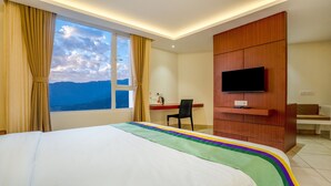 A hotel room with a large bed, a desk, a chair, a TV mounted on a wooden cabinet, and a window with curtains. - Itsy Hotels Meraki Grand (Gangtok)