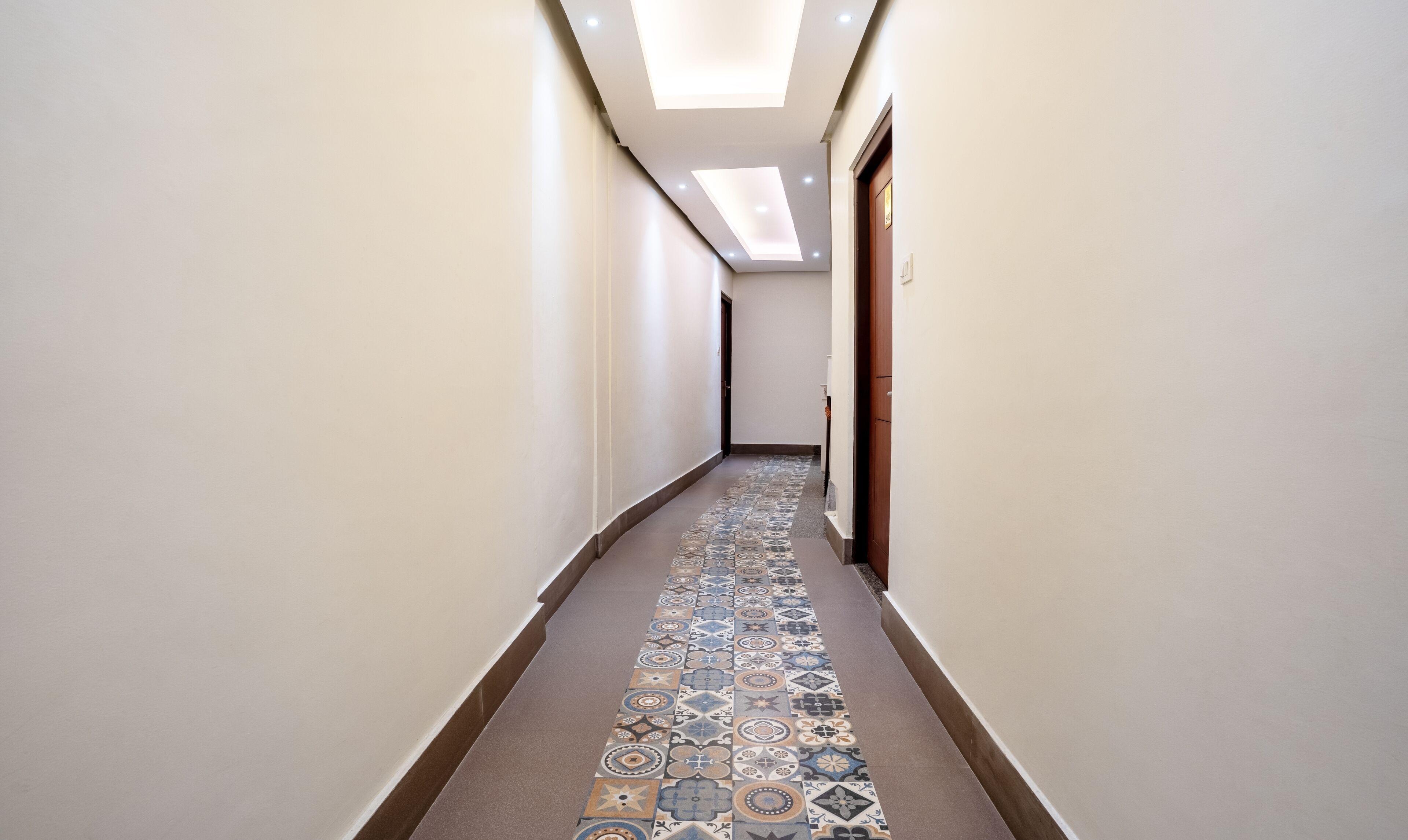 Um corredor com piso estampado, paredes brancas e um claraboia.