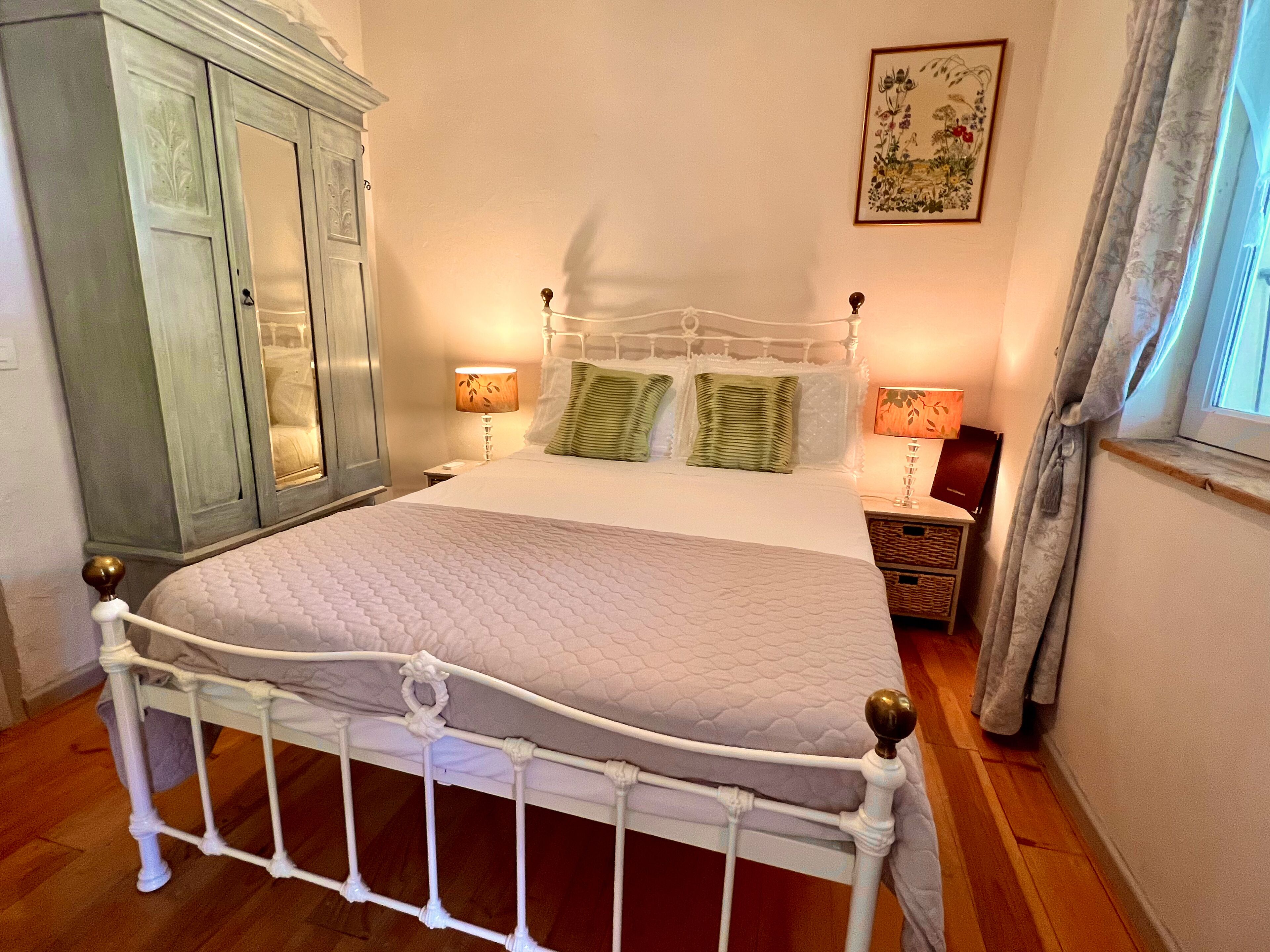 A neatly made bed with a white headboard, a wooden wardrobe, and a framed floral artwork on the wall.