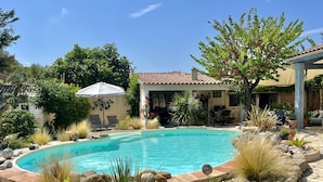 A swimming pool surrounded by rocks and plants, with a patio area and outdoor furniture.