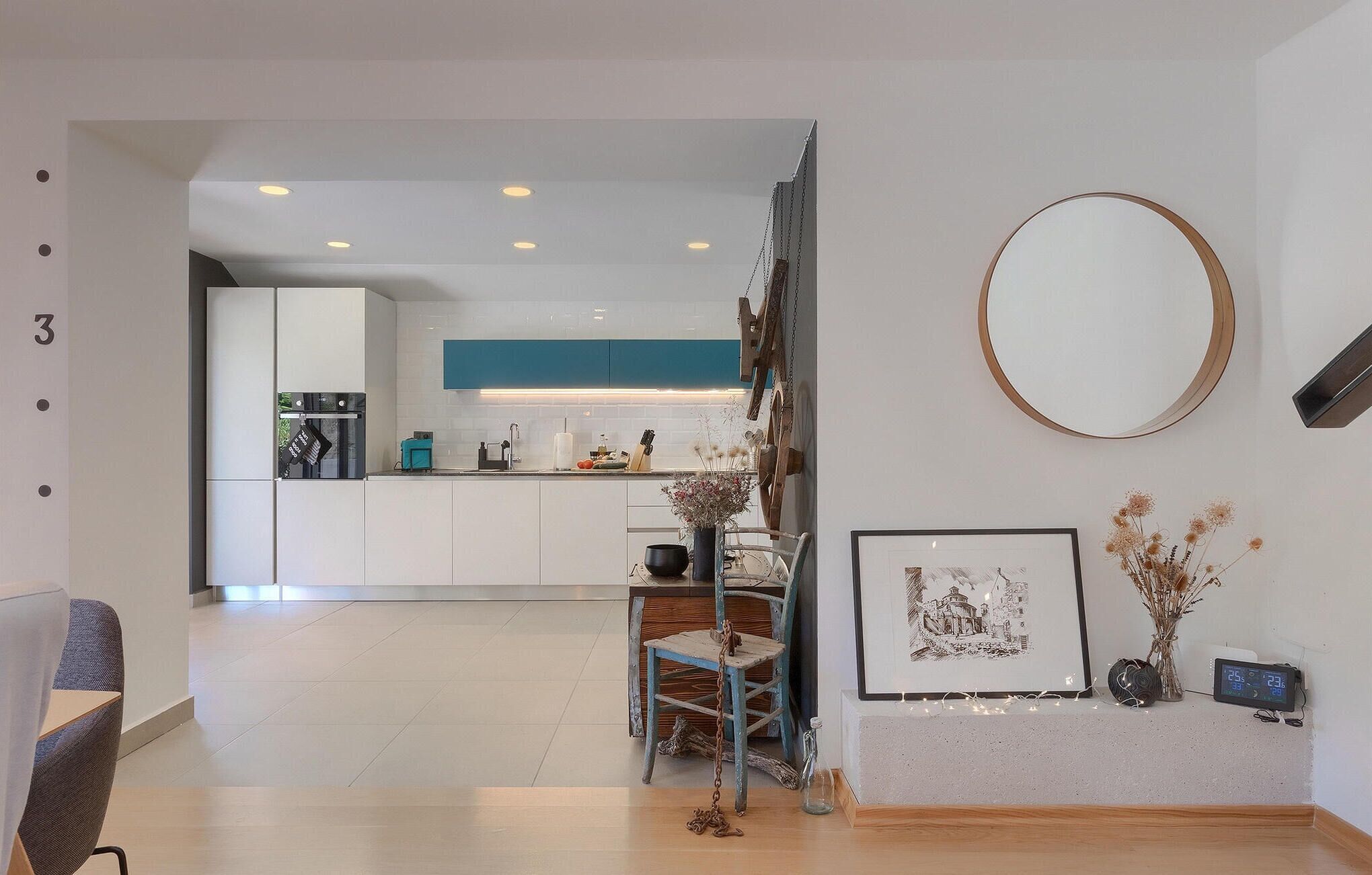 Una cocina moderna con armarios blancos, una pared de acento azul y una silla de madera rústica.