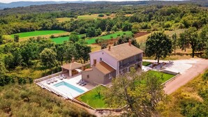 Una casa a due piani con piscina, immersa nel verde e circondata da campi.