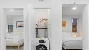 A compact, modern room with a washing machine, a bed, and a small table with a lamp. - Calm Urban Abode steps to Volunteer Park (Seattle)