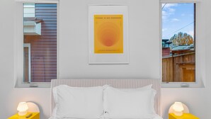 A bedroom with a bed, two bedside tables with lamps, a framed artwork on the wall, and windows with views of a wooden fence and trees. - Calm Urban Abode steps to Volunteer Park (Seattle)