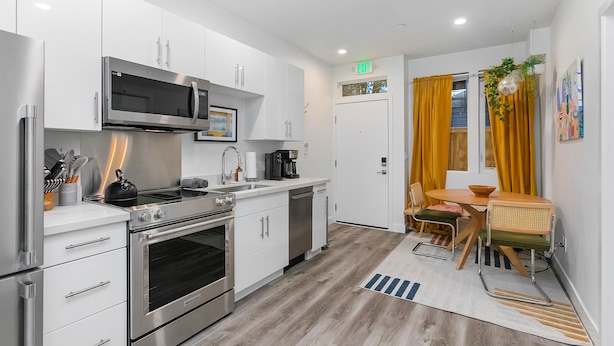 A modern kitchen with stainless steel appliances, white cabinetry, and a dining area with a wooden table and chairs. - Calm Urban Abode steps to Volunteer Park (Seattle)