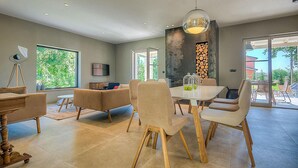 A modern dining area with a large table and chairs, a ceiling light, and a view of the outdoors. - Gorgeous home in Sivati (Sivati)