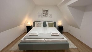 A modern bedroom with a large bed, two bedside tables, and a sloped ceiling. - Modern furnished holiday apartment with two bedrooms and a workspace (Euskirchen)