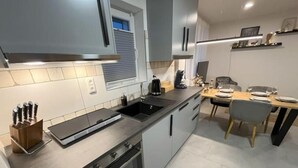 A modern kitchen with a built-in oven, a sink, and a dining area with a table and chairs. - Modern furnished holiday apartment with two bedrooms and a workspace (Euskirchen)
