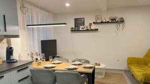 A modern dining area with a wooden table set for four, grey chairs, and a coffee machine on the counter. - Modern furnished holiday apartment with two bedrooms and a workspace (Euskirchen)
