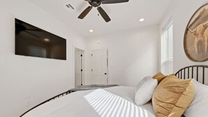 Une chambre à coucher comprenant un lit, un ventilateur de plafond, un téléviseur fixé au mur et une porte donnant sur une autre pièce.
