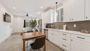 Une cuisine moderne avec des meubles blancs, une table à manger en bois et un ventilateur de plafond.