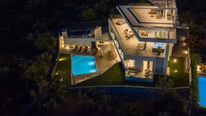 Ein modernes, mehrgeschossiges Haus mit Swimmingpool, Sitzgelegenheiten im Freien und Whirlpool.