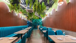 Um restaurante com cabines e mesas, plantas pendentes verdes e iluminação pendente.