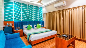Quarto de hotel com cama, sofá azul, mesa de centro de madeira e ar condicionado fixado na parede.