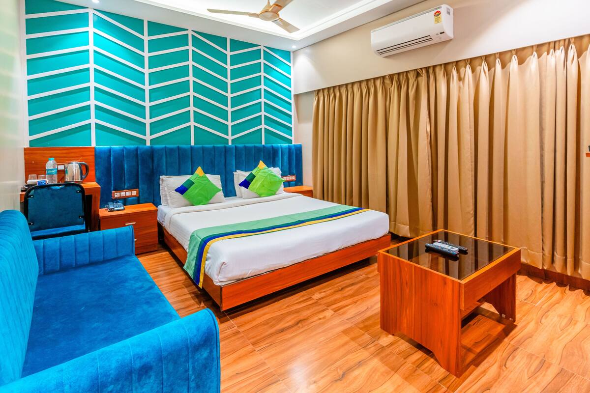 A hotel room with a bed, a blue sofa, a wooden coffee table, and a wall-mounted air conditioner.