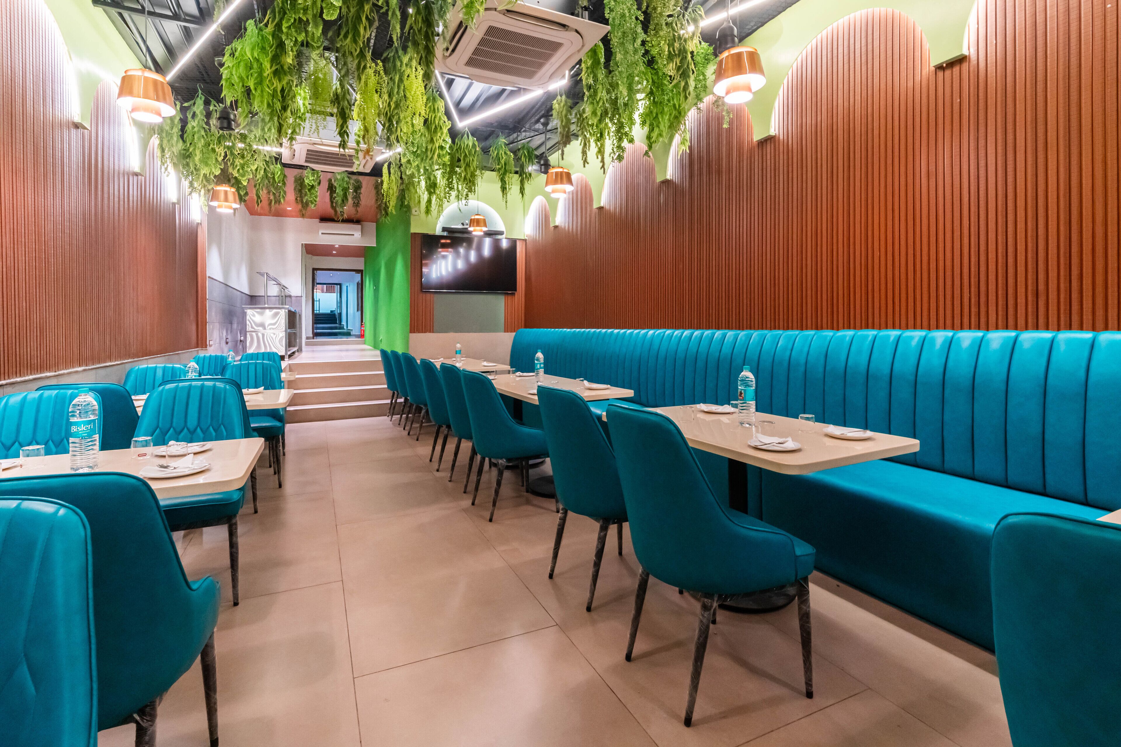 Un restaurante con asientos color turquesa, paneles de madera y plantas colgantes.