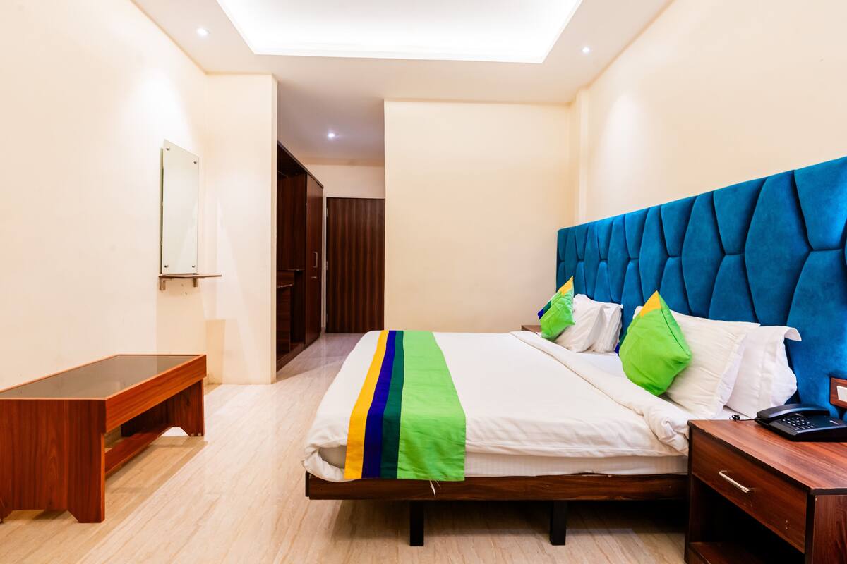 A modern hotel room with a large bed, a bedside table, a desk, and a mirror.