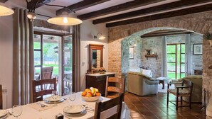 Un comedor con una mesa preparada para cuatro personas, una pared de piedra y una zona de estar acogedora con un sofá y sillones.